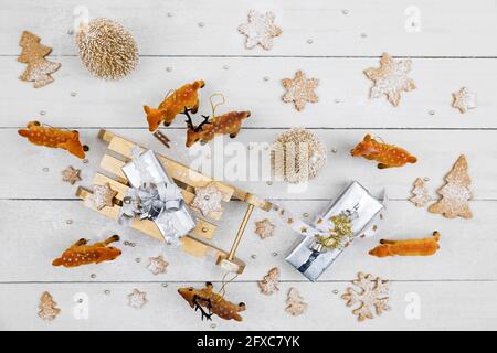 Regali di Natale e slitta giocattolo circondata da cervi giocattolo con biscotti fatti in casa su sfondo di legno bianco Foto Stock