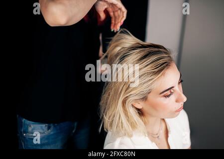 Hairstylist femminile che fa acconciatura del modello biondo in studio Foto Stock