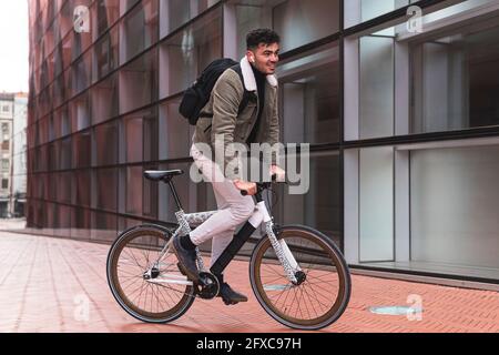 Professionista maschile con zaino in bicicletta all'esterno dell'edificio d'ufficio Foto Stock