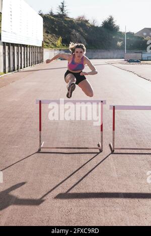 Giovane atleta che salta sopra l'ostacolo durante la giornata di sole Foto Stock
