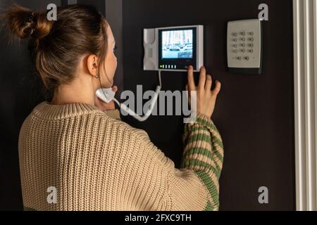 Donna che utilizza un dispositivo intercom a casa Foto Stock