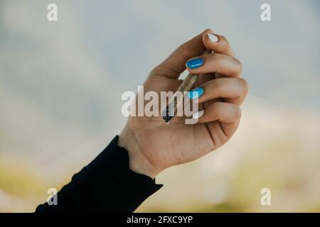 Giovane donna che tiene in mano una sigaretta di marijuana bruciante Foto Stock