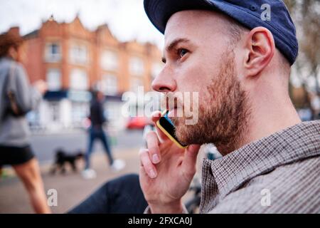 Giovane uomo che guarda via mentre parla con lo smartphone Foto Stock