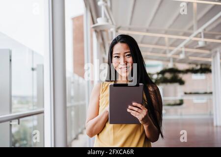 Donna d'affari sorridente che tiene un tablet digitale in ufficio Foto Stock
