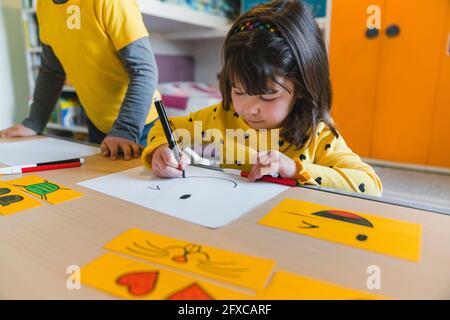 Ragazza che disegna la faccia sorridente sulla carta mentre gioca a casa Foto Stock