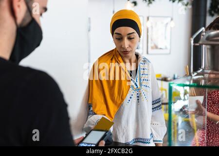 Giovane donna che indossa il copricapo pagando con carta di credito nel ristorante Foto Stock