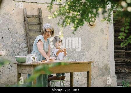 Nonna impastare l'impasto sul tavolo da nipote in cortile posteriore Foto Stock