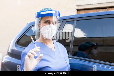 Donna che indossa indumenti da lavoro protettivi mentre si tiene l'iniezione di vaccino COVID-19 in auto Foto Stock