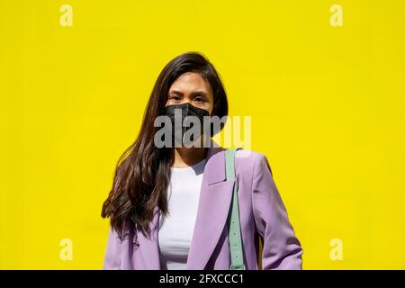 Donna mid adult che indossa una maschera davanti alla parete gialla Foto Stock