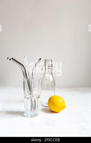 Cannucce riutilizzabili in acciaio inox in vetro e limone su fondo bianco Foto Stock