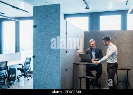 I professionisti maschili discutono sopra il laptop in riunione allo spazio di coworking Foto Stock