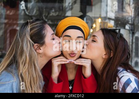 Le amiche baciano la giovane donna indossando un copricapo all'aperto Foto Stock