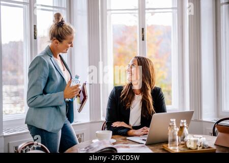 Sorridenti donne d'affari che discutono con una collega in ufficio Foto Stock