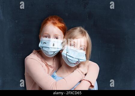 Le sorelle si abbracciano mentre indossano la maschera protettiva per il viso Foto Stock