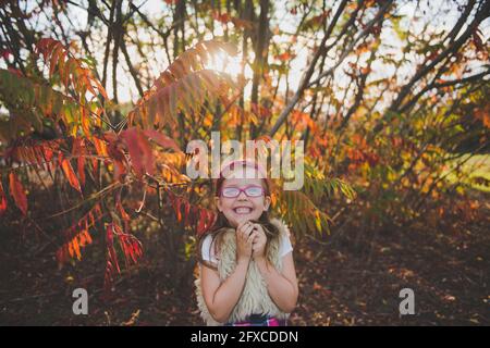 Ragazza sorridente che indossa occhiali di fronte alle piante durante l'autunno Foto Stock