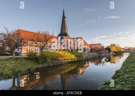 Germania, Altes Land, Jork, edifici a graticcio e chiesa di San Nikolai che si riflette nel canale Foto Stock