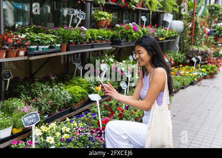 Donna che fotografa le piante attraverso smartphone in asilo nido Foto Stock