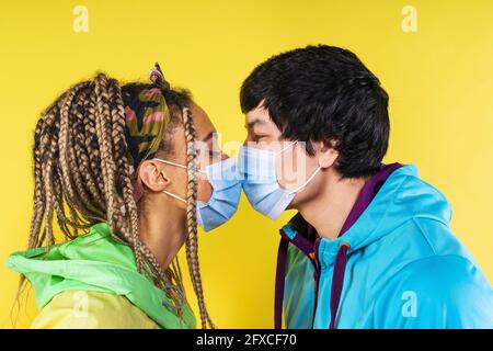 Coppia con maschera viso baciarsi l'un l'altro da sfondo giallo Foto Stock