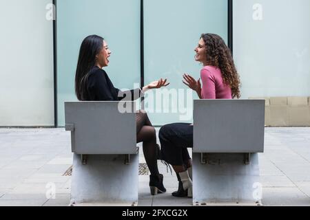 Le giovani donne che parlano tra loro mentre si siedono sulla panchina Foto Stock