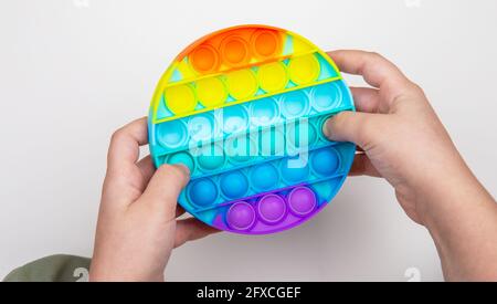 Bambino che gioca con il colorato pop it fidget. Primo piano le mani dei bambini che giocano con il colorato poppit giocattolo in casa Foto Stock