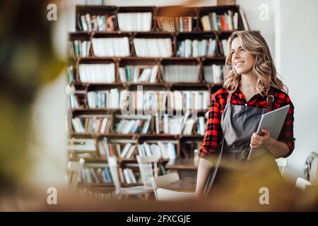 Cameriera femminile premurosa che tiene un tablet digitale e un vassoio da servire presso la caffetteria Foto Stock