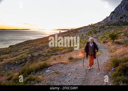 Donna anziana con pali escursionistici sul sentiero vicino al mare Adriatico a Omis, Dalmazia, Croazia Foto Stock