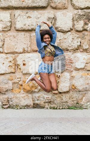 Donna con braccia sollevate che salta di fronte al muro Foto Stock
