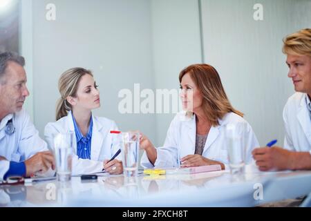 Donna matura che gesturing mentre discute con gli operatori sanitari durante la riunione in ospedale Foto Stock