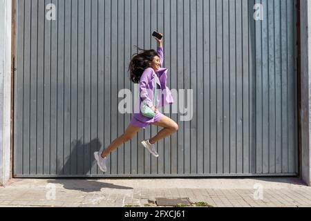 Donna entusiasta che salta da una parete grigia Foto Stock