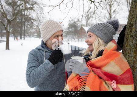 Una coppia sorridente che beve tè in tazza durante l'inverno Foto Stock