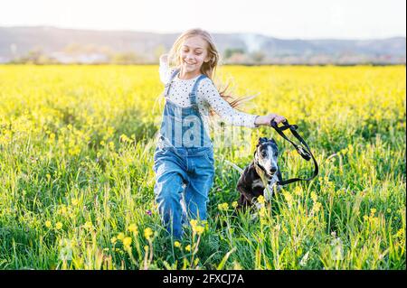 Ragazza sorridente che corre con il cane in campo agricolo Foto Stock
