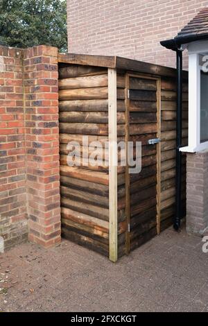 Capannone di legno di recente costruzione come una capannone di attrezzi o area di deposito di ceppo costruito contro una parete circostante di mattone. Foto Stock