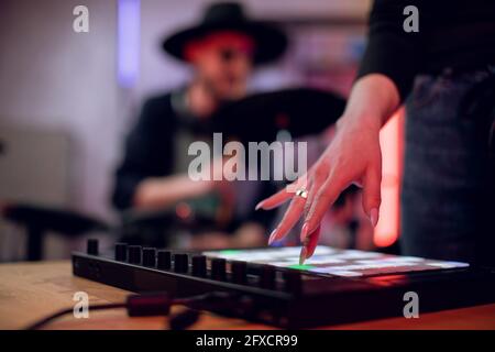 Primo piano della tavola di mixaggio a contatto con la mano femminile per creare una canzone di successo in studio. Sfocatura sfondo di artista maschile che suona su tamburi elettronici. Registrazione musicale. Foto Stock