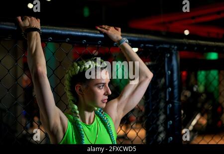 Pugilato ring girl pone prima di una lotta nell'arena della scena ottagonale, vista attraverso la rete metallica. Donna attraente negli sport di mixed martial Foto Stock