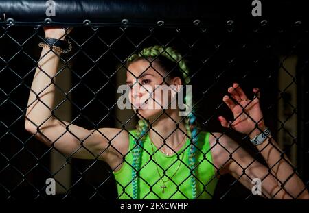 Pugilato ring girl pone prima di una lotta nell'arena della scena ottagonale, vista attraverso la rete metallica. Donna attraente negli sport di mixed martial Foto Stock