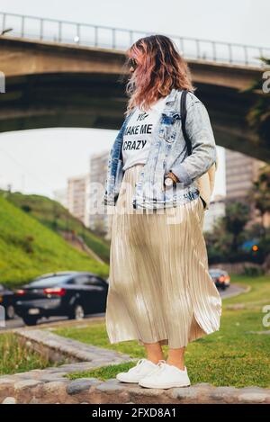 Vestita alla moda, femminista a tutta lunghezza con un ponte sullo sfondo. Immagine verticale Foto Stock