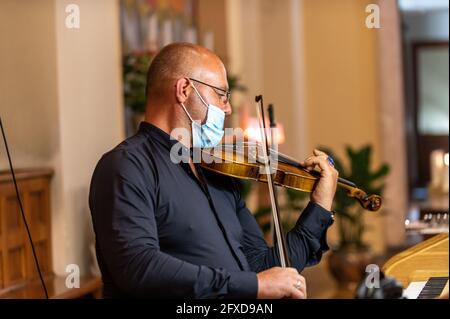 violinista in chiesa con maschera medica che suona violino Foto Stock