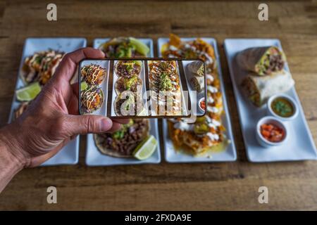 L'uomo scatta una foto dei piatti messicani sul tavolo da ristorante Foto Stock