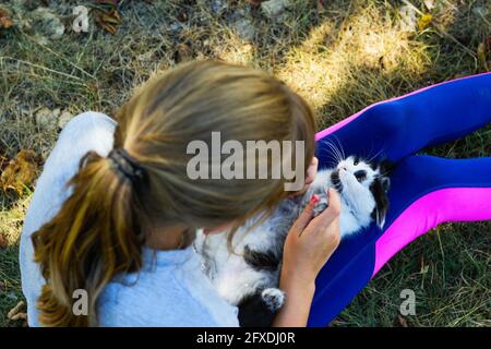 Defocus bambina bionda che gioca con gatto, bianco e nero piccolo gattino relax. Natura giallo estate sfondo. Ragazza stroking animale domestico. Servizio bambini Foto Stock