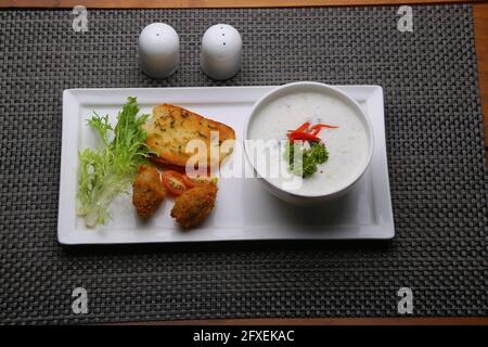 Crema di funghi zuppa disposta in una ciotola bianca con pane tostato e insalata di verdure fresche come contorno sistemato su una tavola da portata bianca con colore grigio Foto Stock