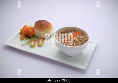 Zuppa di pollo di Manchow, guarnita con verdure e tagliatelle arrangiate in un ciotola bianca con texture o sfondo bianco Foto Stock