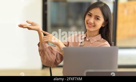 Ritratto a mezza lunghezza di punta femminile e palmo aperto con spazio per la copia mentre si è seduti in ufficio Foto Stock