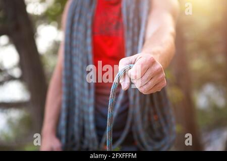 Un arrampicatore maschio di aspetto caucasico con una corda avvolta in mano. Avvolgimento della fune, nodo, stoccaggio delle attrezzature. Mano in magnesia bianca. Rosso sport Jerse Foto Stock