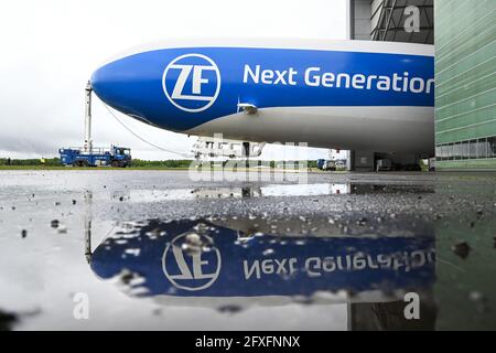 Friedrichshafen, Germania. 27 maggio 2021. La Zeppelin NT (Nuova tecnologia) viene estratta dall'hangar da un camion in modo che l'aeronave possa decollarsi per il suo volo stampa nel pomeriggio. Lo Zeppin stesso si riflette in una pozza davanti all'hangar. La Zeppelin NT inizierà la sua stagione venerdì 28.05.2021. Credit: Felix Kästle/dpa/Alamy Live News Foto Stock