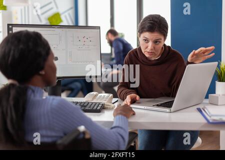 Imprenditore africano handicappato non valido in sedia a rotelle lavorare con il project manager calcolare il profitto sul laptop, scrivere sul pc, analizzare i documenti finanziari seduti in start-up società finanziaria. Foto Stock