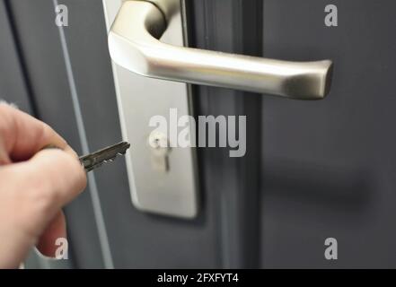 Una mano che tiene una chiave per inserire una chiave nella serratura della porta. Sbloccaggio del blocco di sicurezza. Foto Stock