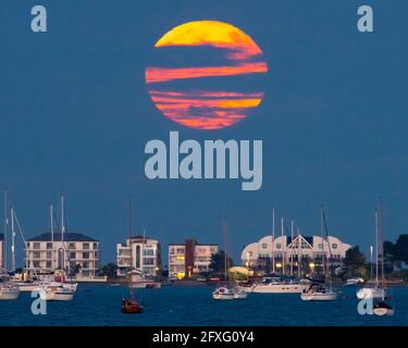 Poole, Dorset, Regno Unito. 26 maggio 2021. Regno Unito Meteo. La luna super piena fiore è oscurata dalle nuvole che sale da dietro fila milionari a Sandbanks a Poole in Dorset. Picture Credit: Graham Hunt/Alamy Live News Foto Stock