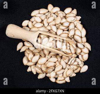 Vista dall'alto della paletta di legno sul mucchio di zucca non semigreggio semi su piastra nera Foto Stock