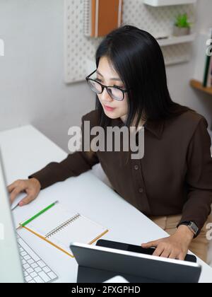 Vista dall'alto della lavoratrice da ufficio femminile con occhiali che si concentrano il suo lavoro con computer e forniture per ufficio Foto Stock