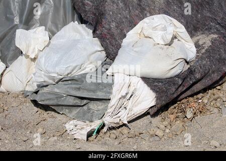 Mazzo di sacchi di sabbia bianchi nuovi e vecchi, rotti e strappati, con protezione spessa in nylon scuro e copertura in tessuto geotessile per protezione temporanea dalle inondazioni Foto Stock